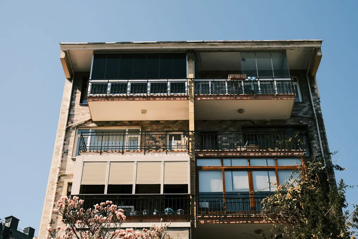 A modern apartment building facade with balconies above flowering shrubs.