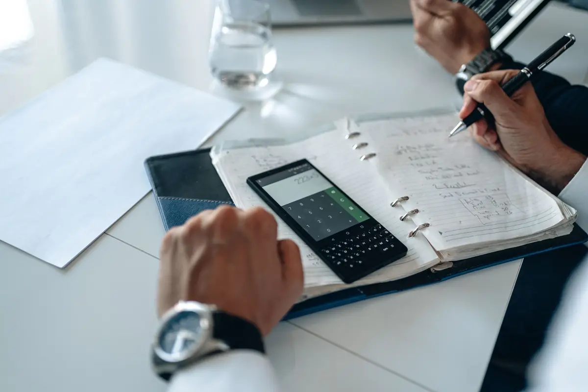 A desk with an open notebook, a calculator and a pen mid-sentence.