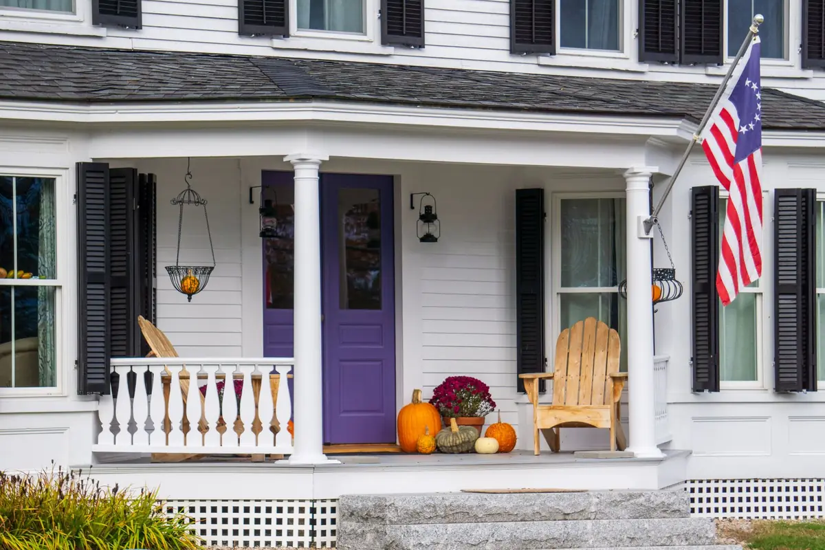 A wooden clapboard porch with turned posts and autumn planting on the steps.