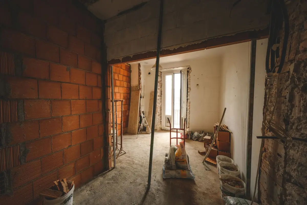 A partly renovated room with exposed brick, bare joists and materials stacked against a wall.