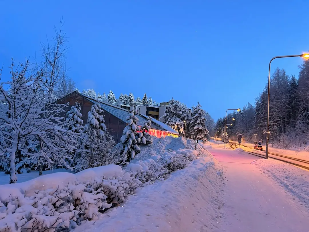 A snow-covered path beside bare trees and a building at dusk.